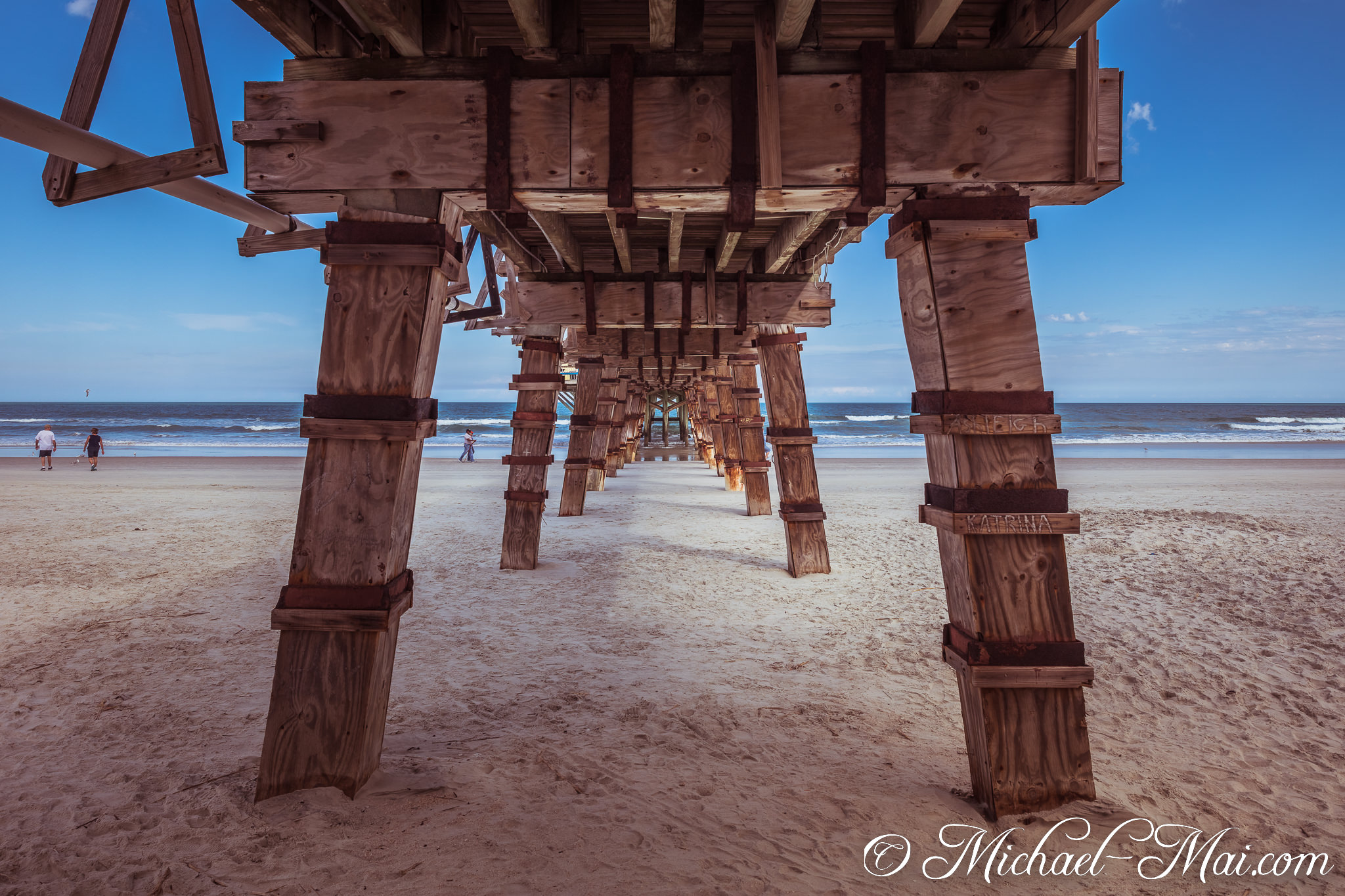 Underneath the pier, robust wooden columns lead the eye down the sandy beach to the horizon. | Daytona Beach Shores, Florida, United States