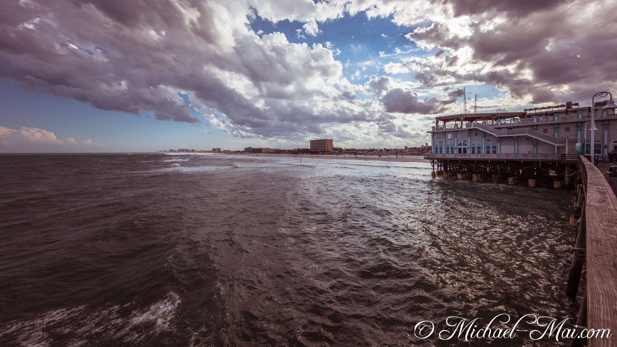 Dramatic clouds loom over dark, choppy waters next to a sturdy pier structure. | Daytona Beach, Florida, United States