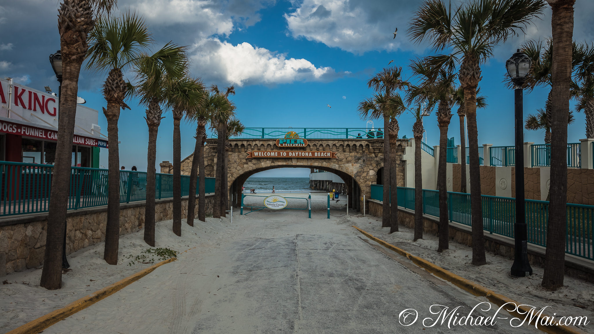 Iconic stone archway and palm trees greet beach-goers arriving at the ocean's edge. | Daytona Beach, Florida, United States