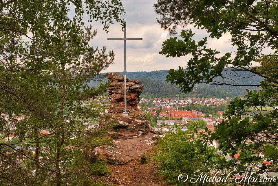 From a scenic overlook, a cross rises above a valley town and distant forests. | Hauenstein, Germany