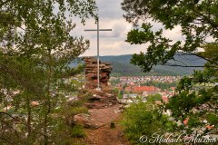 From a scenic overlook, a cross rises above a valley town and distant forests. | Hauenstein, Germany