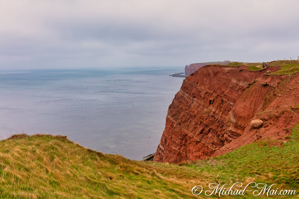 Majestic red cliffs dramatically plunge into the vast ocean under soft, cloudy light.
