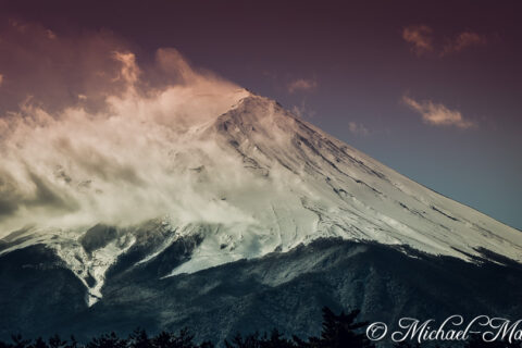 Dynamic clouds embrace the snow-capped peak of Mount Fuji under a dramatic gradient sky. | Mount Fuji, Japan