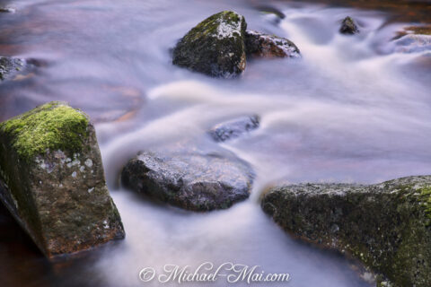 Gliding water creates a soft blur around moss-kissed river rocks.