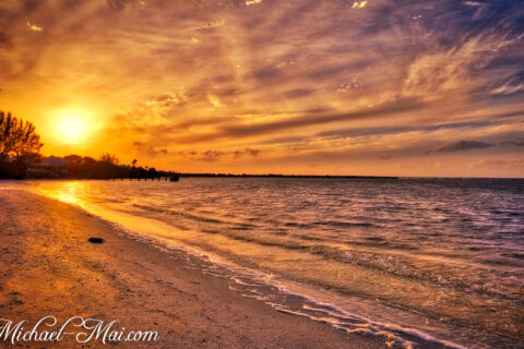 A brilliant sunset paints the sky with fiery hues, illuminating the beach and waves.