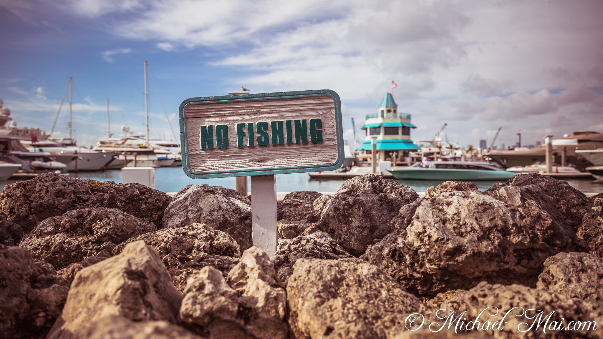 Among rugged rocks, a "NO FISHING" sign prohibits activity near the bustling yacht marina. | Miami Beach, Florida, United States