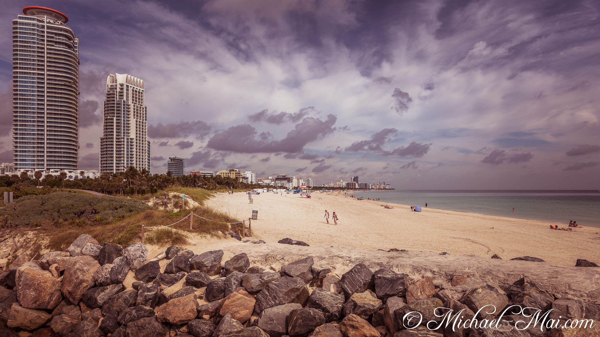 Beach life unfolds on warm sand, framed by towering city buildings and cloudy skies. | Miami Beach, Florida, United States