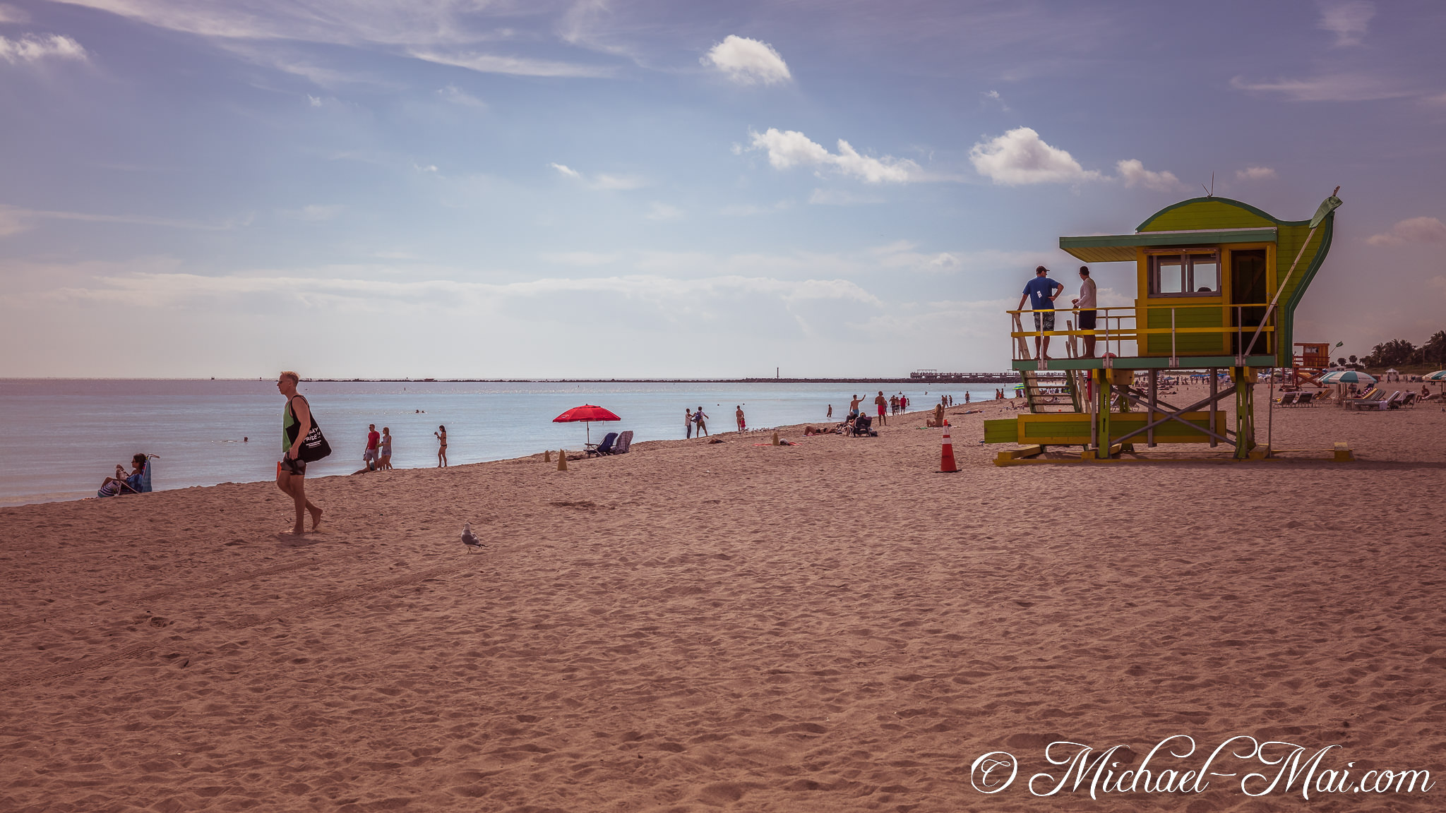 Bright green lifeguard tower watches over beachgoers enjoying a sunny Miami day. | Miami Beach, Florida, United States