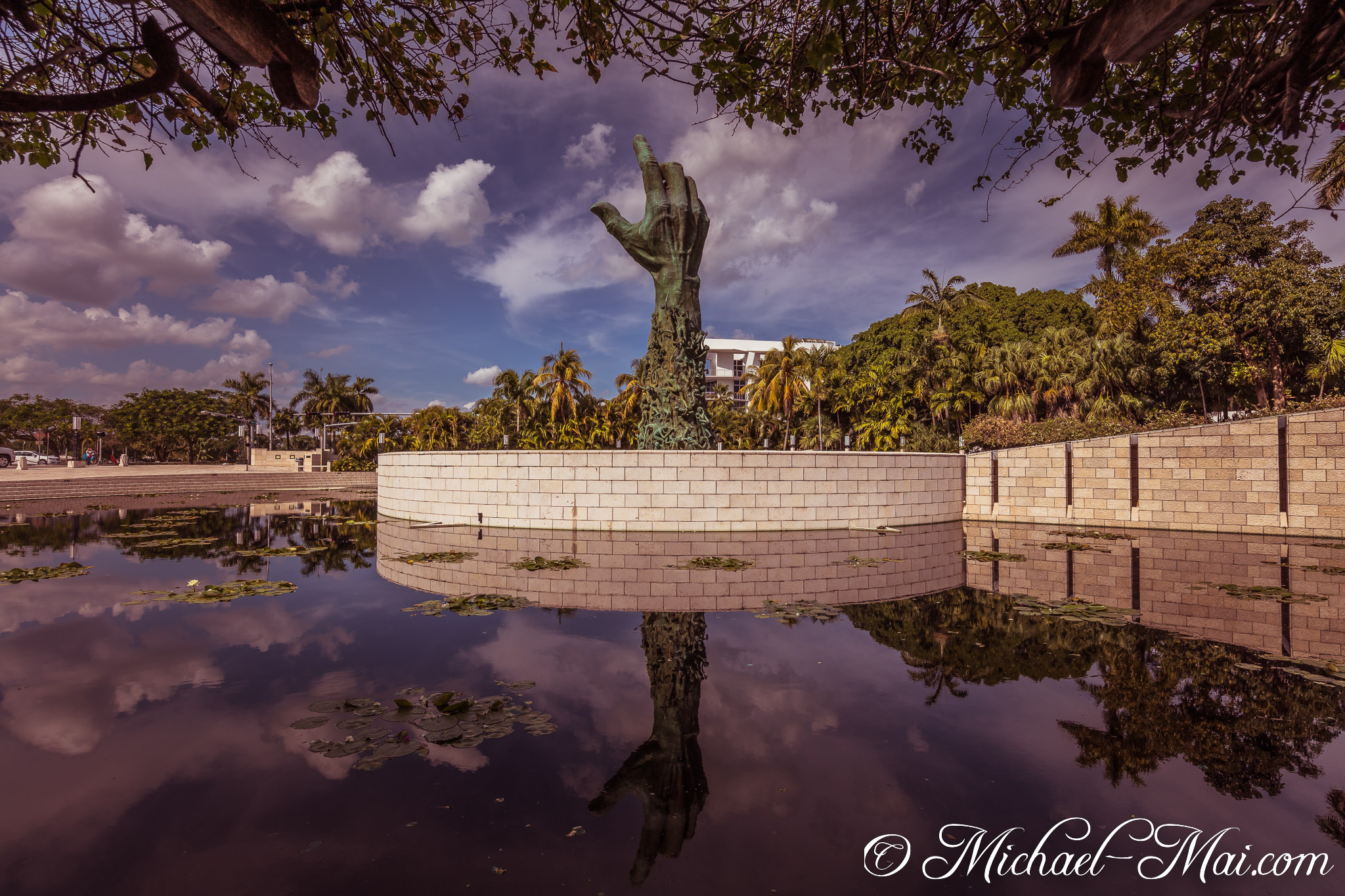 Iconic hand sculpture powerfully reaches for the heavens, mirrored in still dark waters. | Miami Beach, Florida, United States
