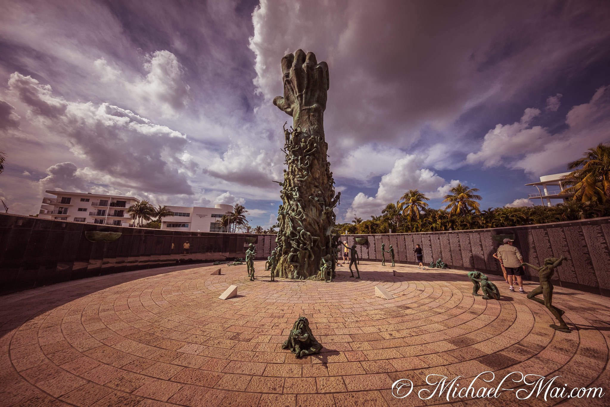 Bronze figures gather around the soaring central hand, memorializing profound suffering under dynamic clouds. | Miami Beach, Florida, United States