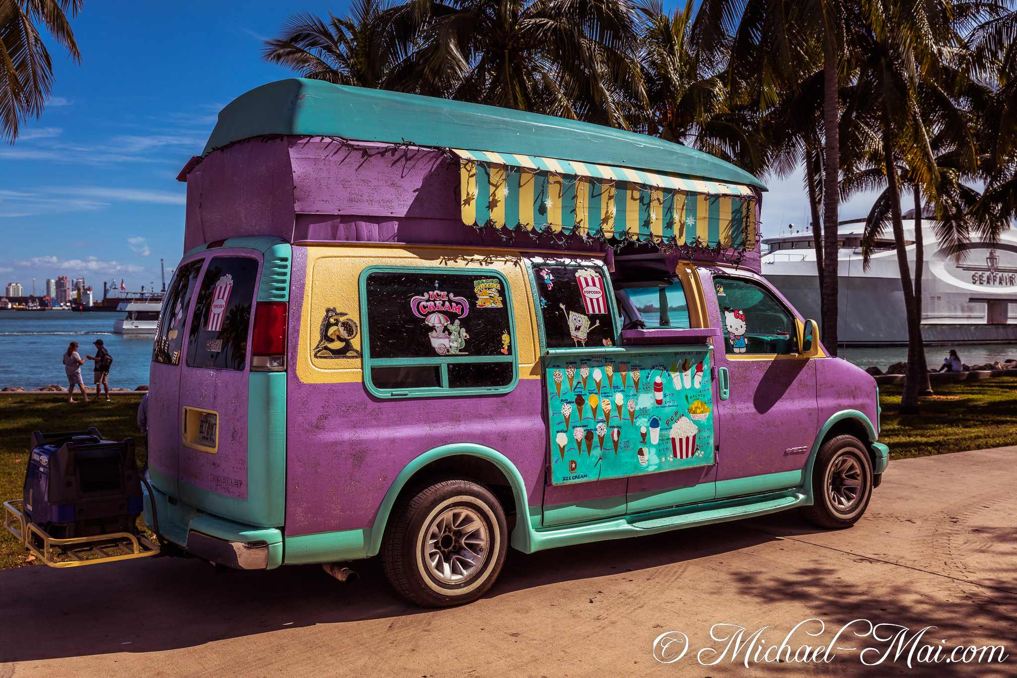 Colorful ice cream van with whimsical decals brightens the Miami waterfront under palm trees. | Miami, Florida, United States