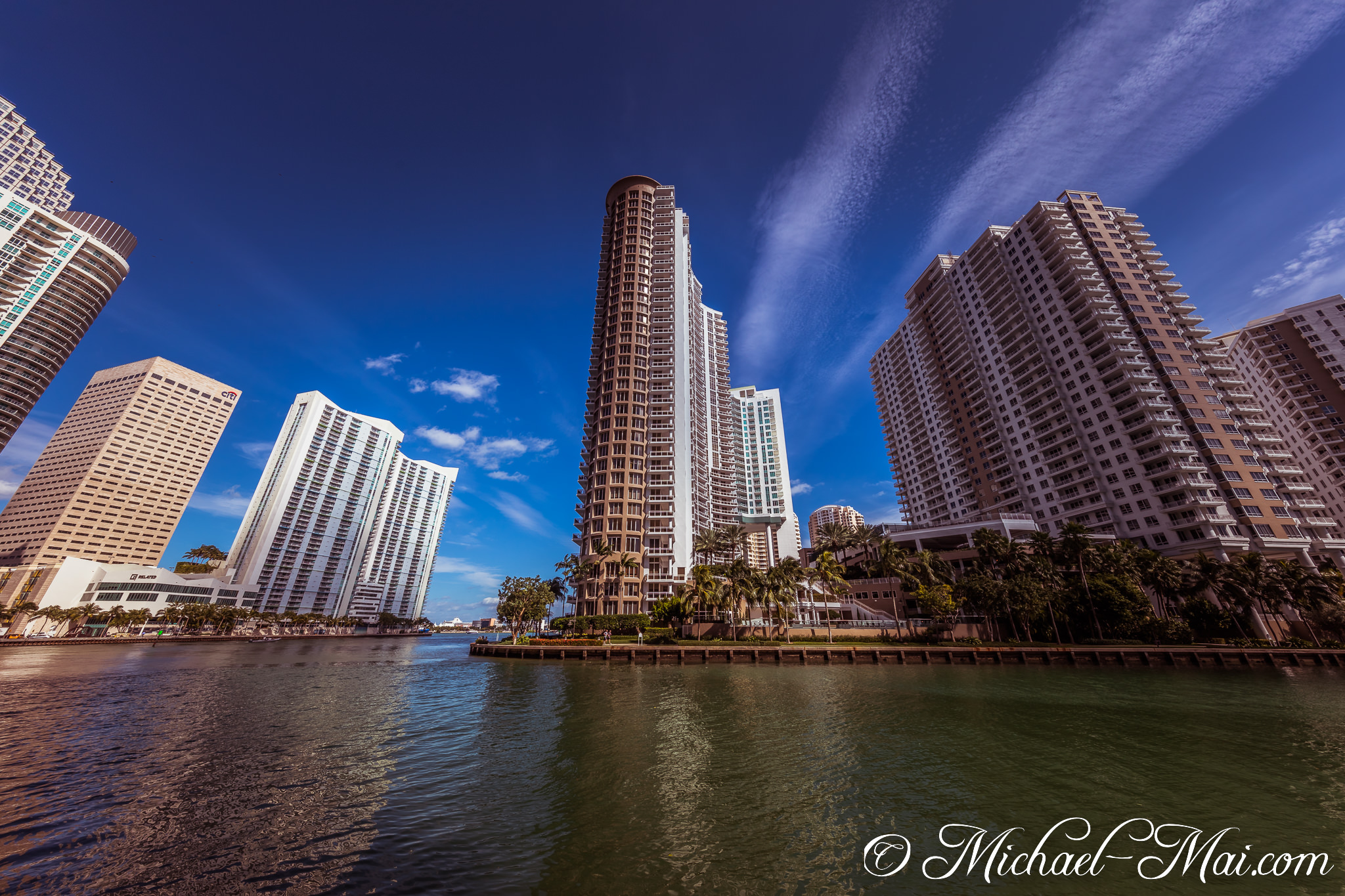 Striking skyscrapers line the waterway, reflecting the bright blue sky and scattered clouds. | Miami, Florida, United States