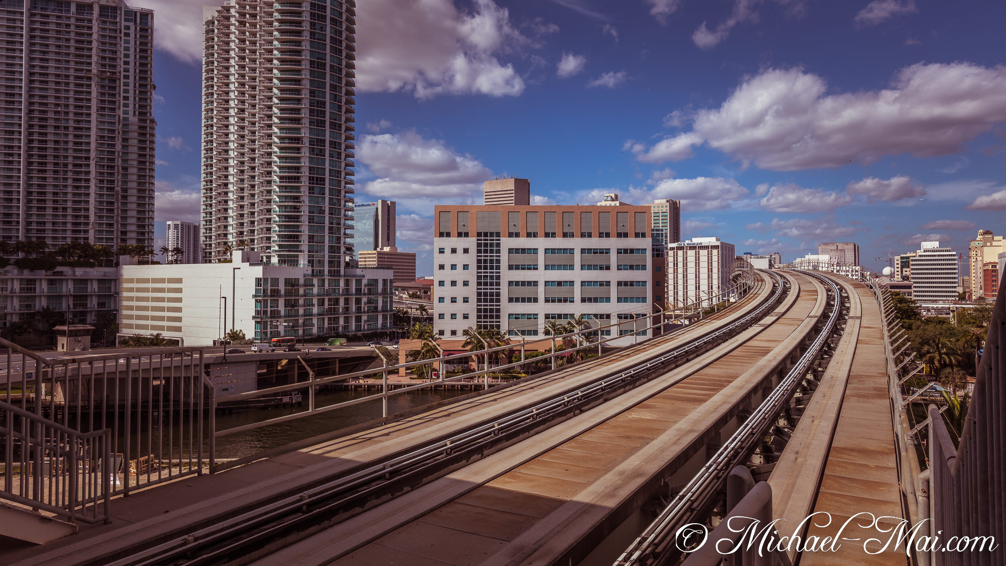 Curving transit tracks wind through Miami's high-rise architecture beneath a cloud-strewn sky. | Miami, Florida, United States