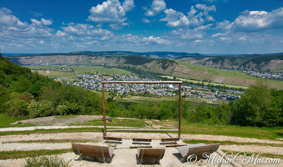 Wooden frame outlines a vast river valley with a village nestled among terraced vineyards.