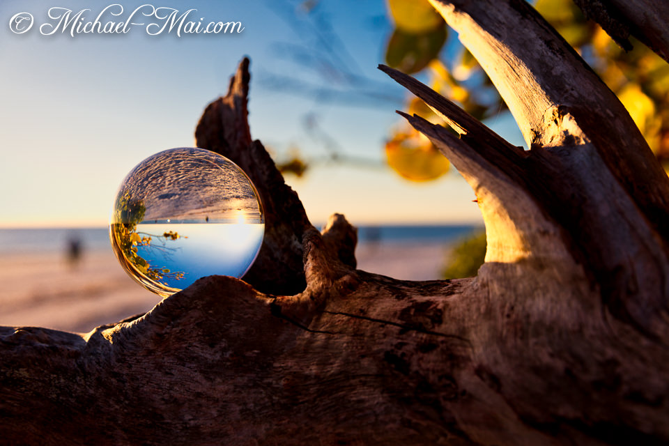 Glass sphere on weathered wood captures an inverted, luminous beach sunset.