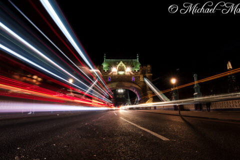 Road traffic transforms into bright, energetic light trails towards Tower Bridge.
