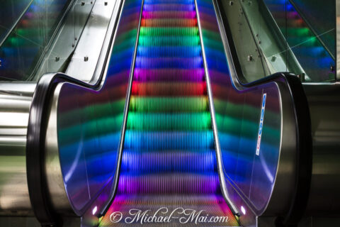 Rainbow lights brilliantly illuminate the rhythmic steps of a modern escalator.