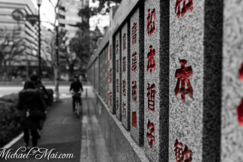 Bold red kanji characters stand out on a stone wall overlooking a muted city street.