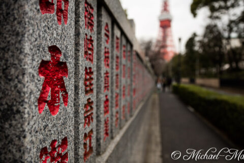 Textured granite frames vibrant red characters, their path leading to the iconic Tokyo Tower.