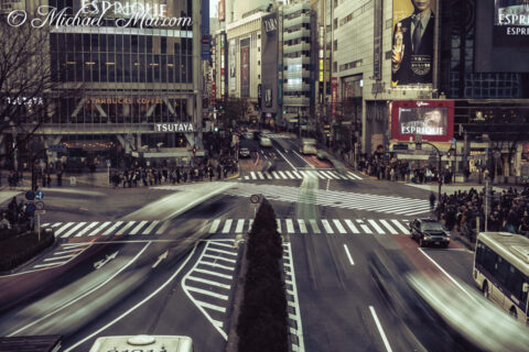 Motion blurs vehicles into dynamic light trails across a bustling city intersection. | Shibuya Crossing, Tokyo, Japan