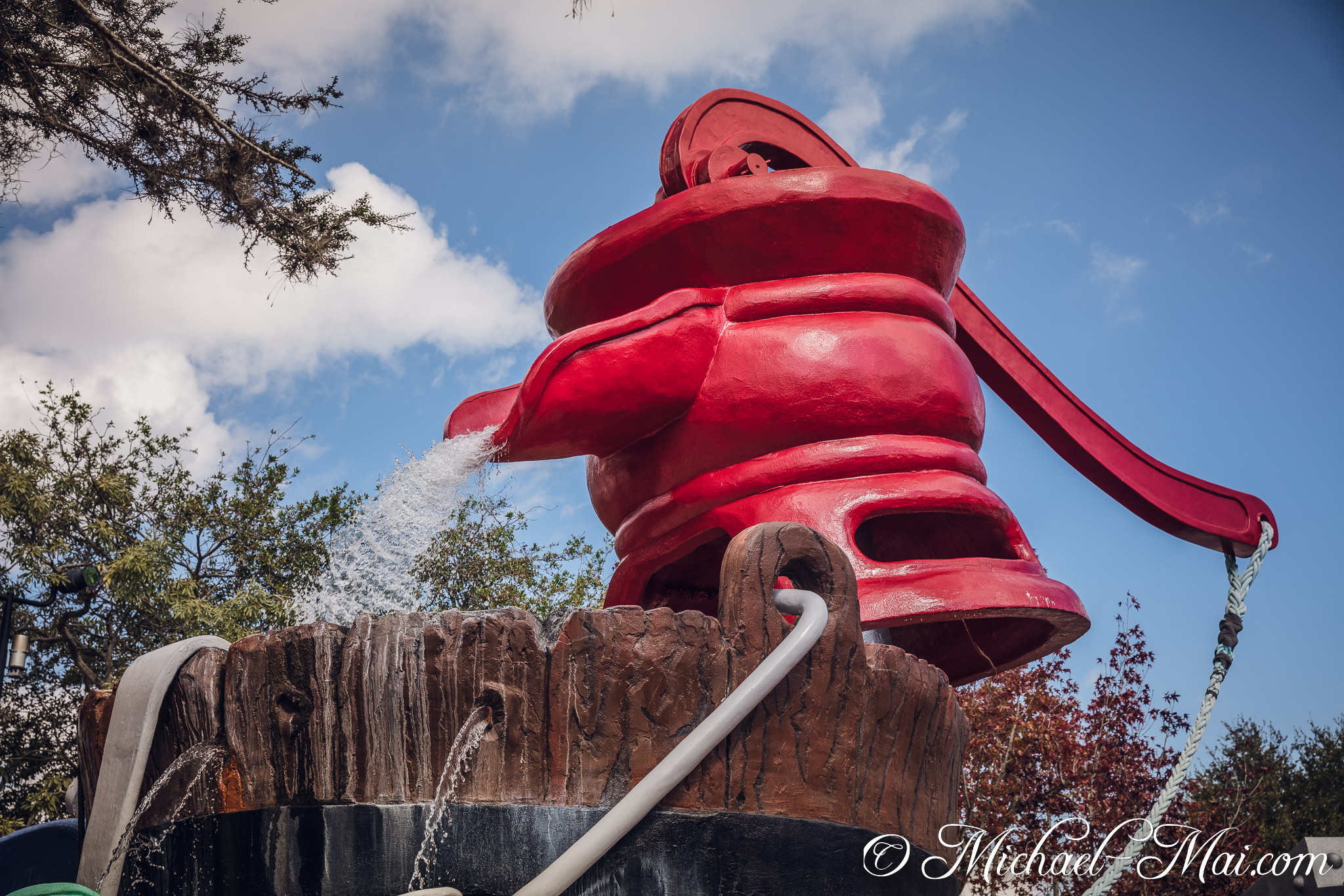 Water dramatically spills from an enormous red pump into a textured basin. | Orlando, Florida, United States