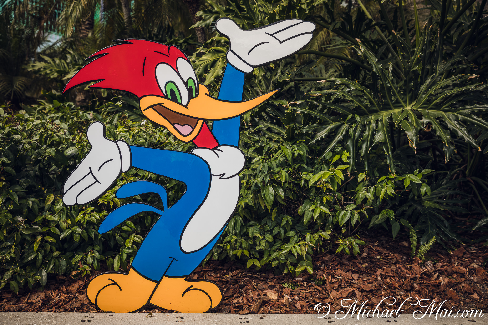 Animated Woody Woodpecker cheerfully gestures, welcoming all amidst the park greenery. | Orlando, Florida, United States
