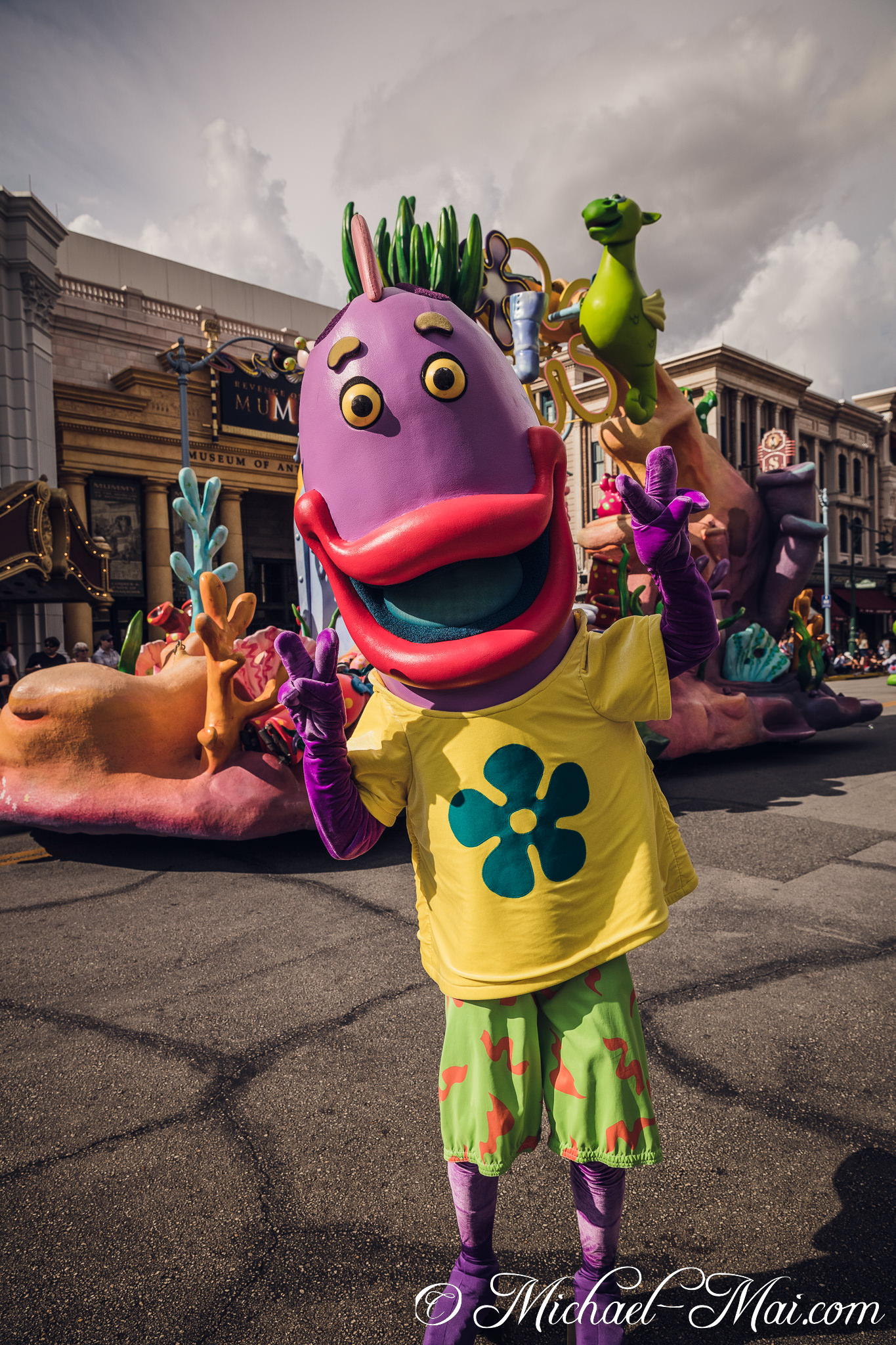 Smiling widely, a whimsical purple character greets guests with peace signs. | Orlando, Florida, United States