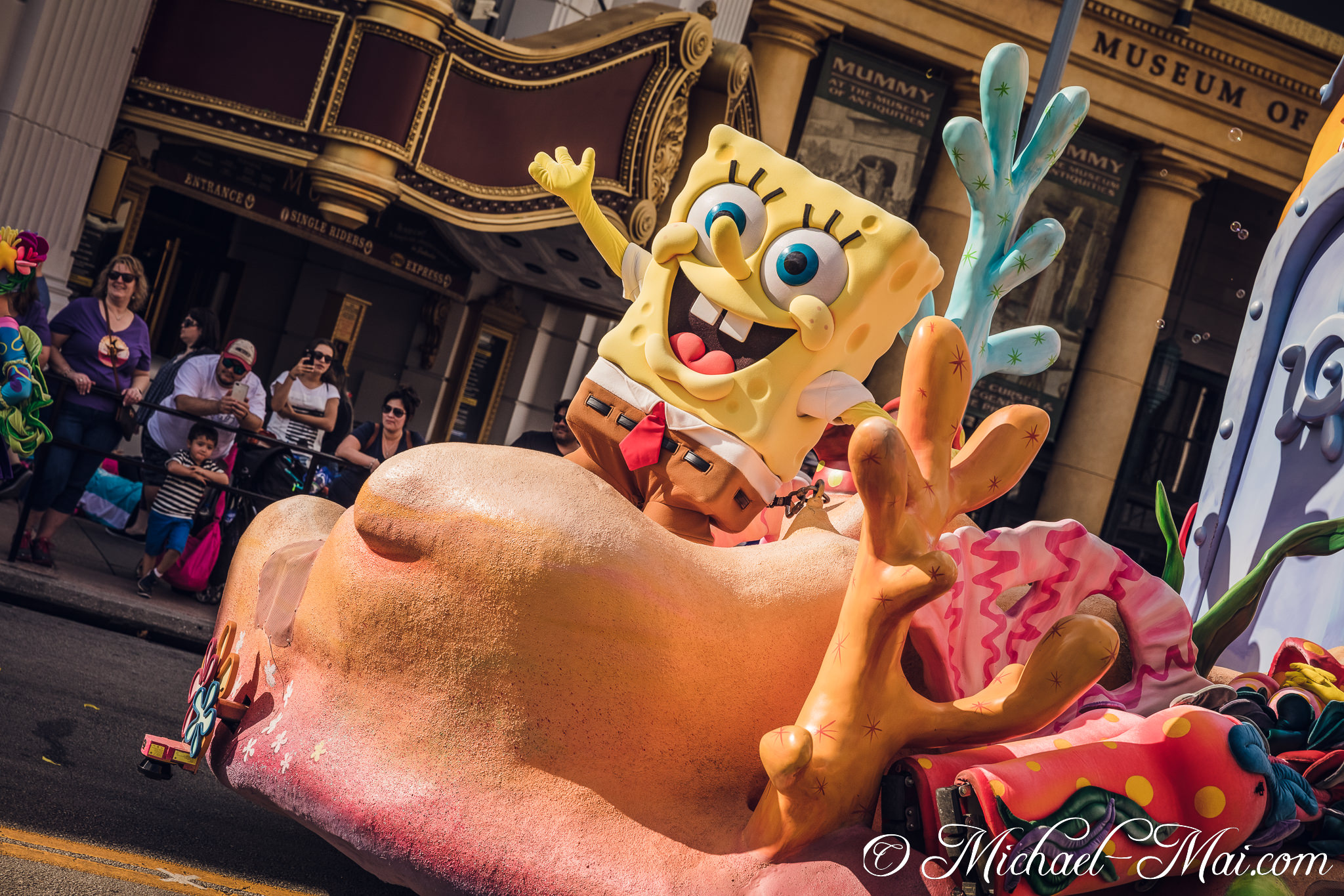Waving Spongebob on a colourful float glides past onlookers and historic architecture. | Orlando, Florida, United States
