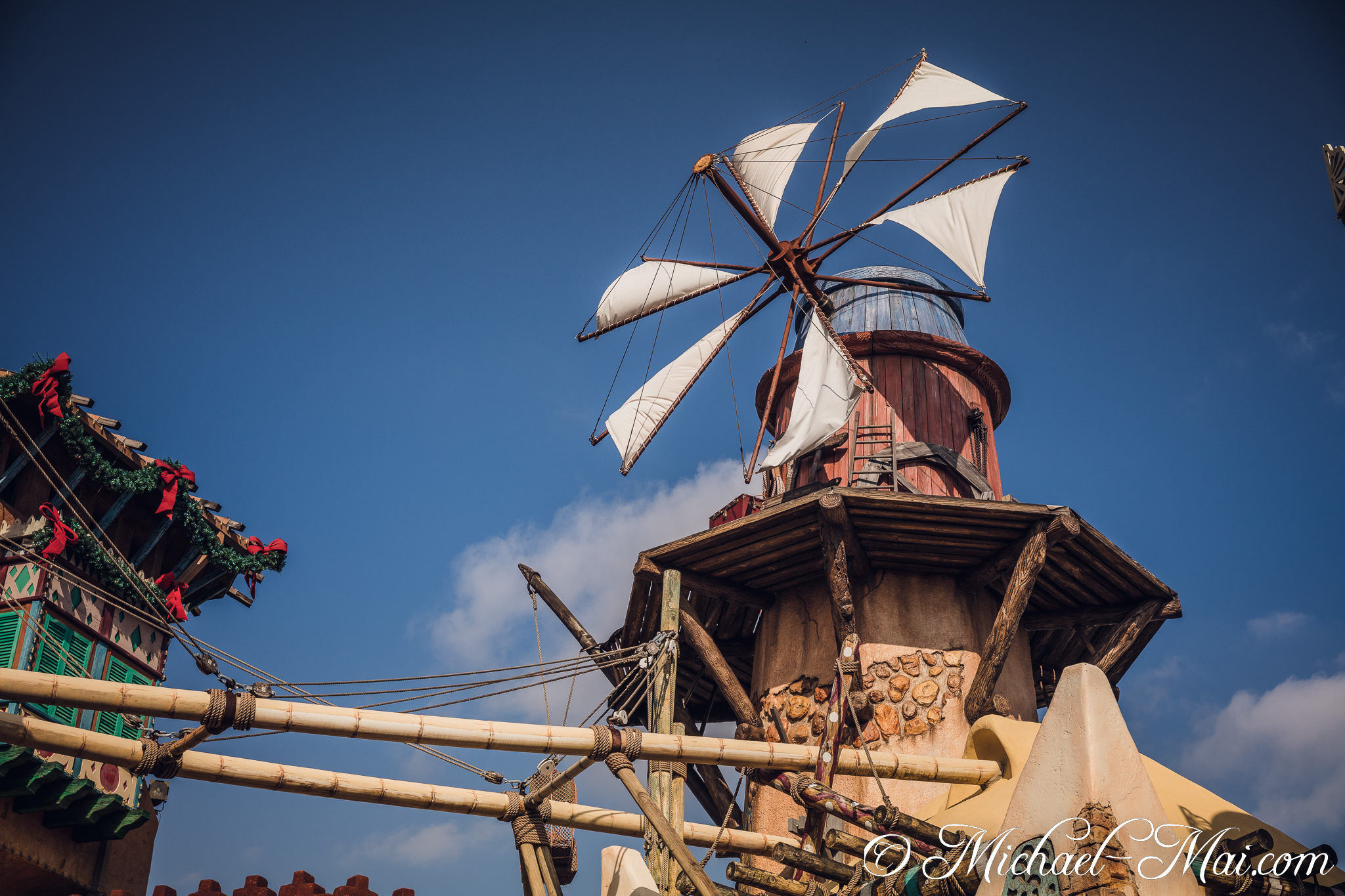 Weathered windmill with canvas sails and festive decorations under a crisp blue sky. | Orlando, Florida, United States