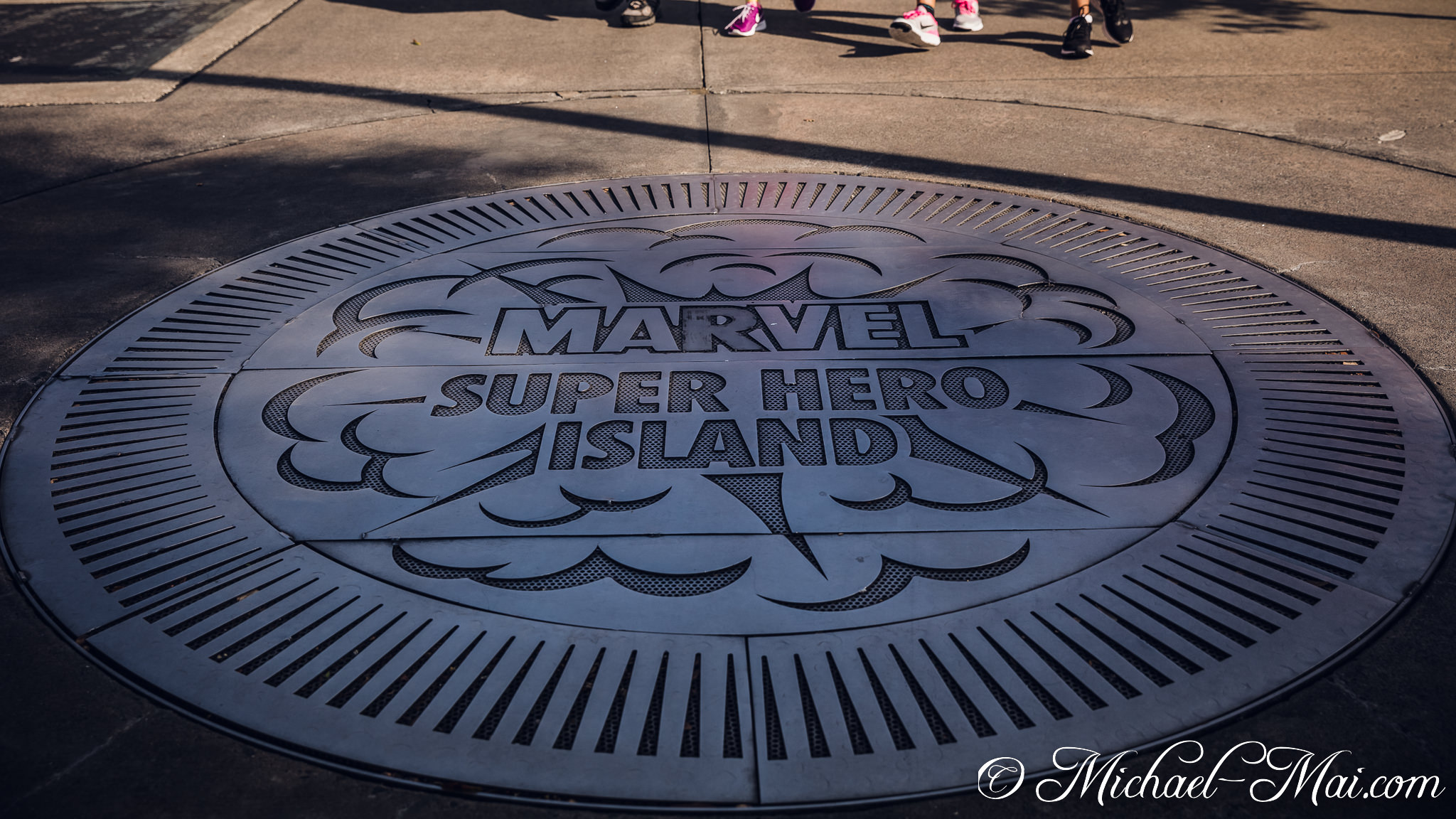 Sunlight illuminates the bold "Marvel Super Hero Island" emblem on the pavement. | Orlando, Florida, United States