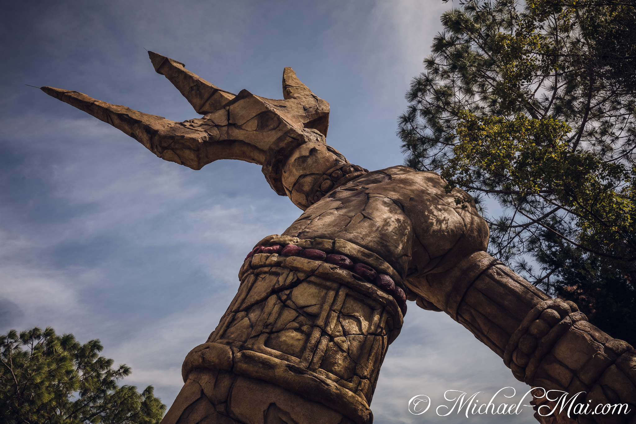Upward gaze reveals a colossal, cracked stone trident reaching towards the clouds. | Orlando, Florida, United States